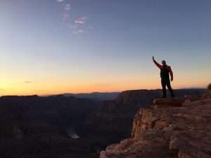 man waving to camera from canyon ledge