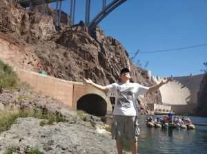 person looking up with arms outstretched next to Hoover Dam