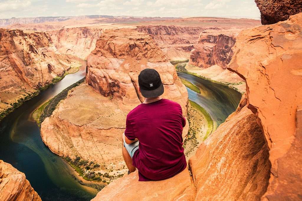 man in red shirt sitting on Horseshoe Bend overlook