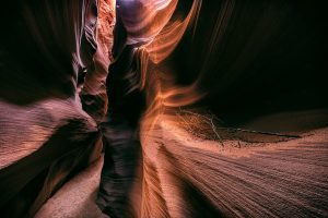 Warm-toned, swirling rock formations of Antelope Canyon with a glimpse of sky above.