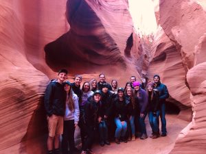 Group of tourists inside a narrow, wavy red sandstone canyon.