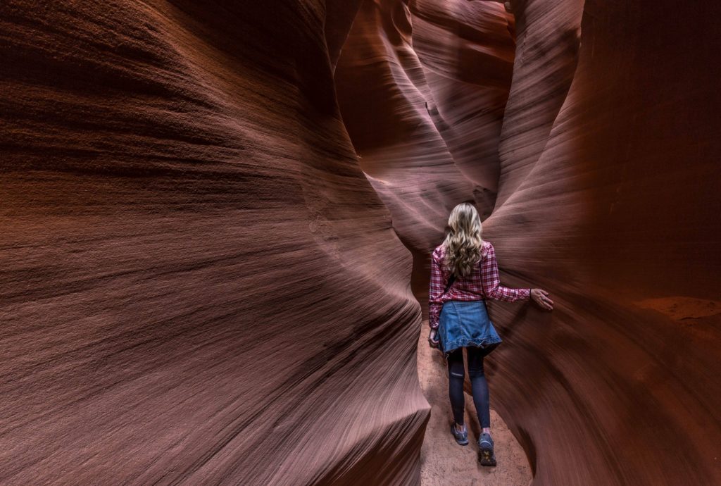 Person exploring a narrow, wavy, red sandstone canyon.