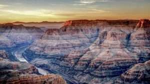 Majestic view of the Grand Canyon at sunset, showcasing layered rock formations and the winding Colorado River in the foreground.